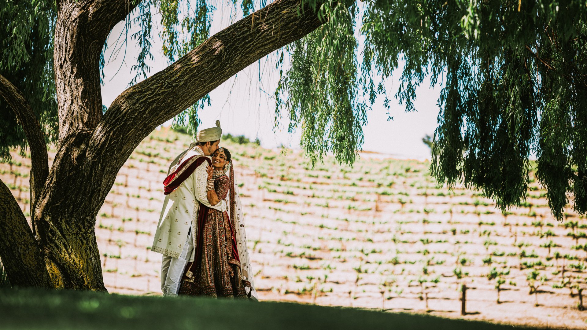 Couple in traditional wedding attire standing beneath vineyard trees, reflecting the diverse private event venues at Léal Vineyards.