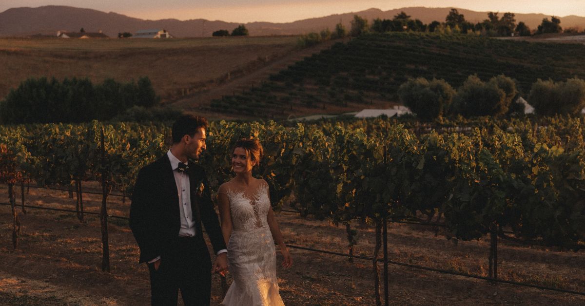 Bride and groom walking through autumn vineyard at sunset with vineyard wedding packages