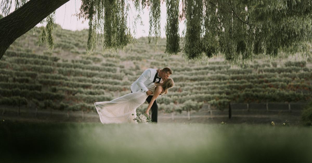 Bride and groom sharing a kiss under a tree at a vineyard wedding venue in Hollister CA